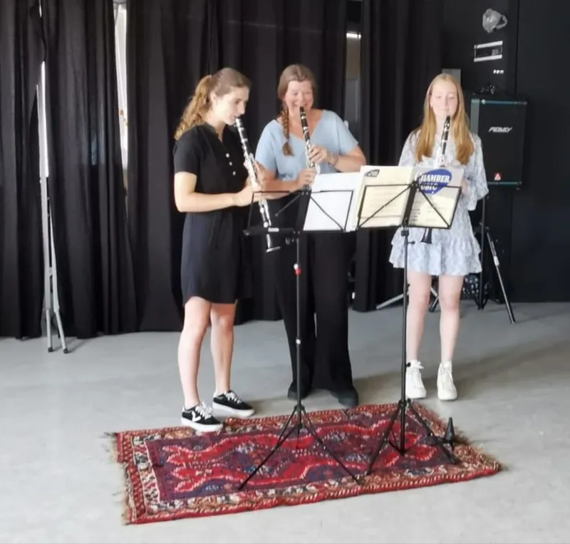Drie klarinettistes spelen samen achter muziekstandaards op een kleed